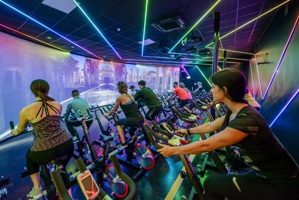 Immersive cycling studio at Westmanstown Club showcasing a large video wall and surround digital lighting strips